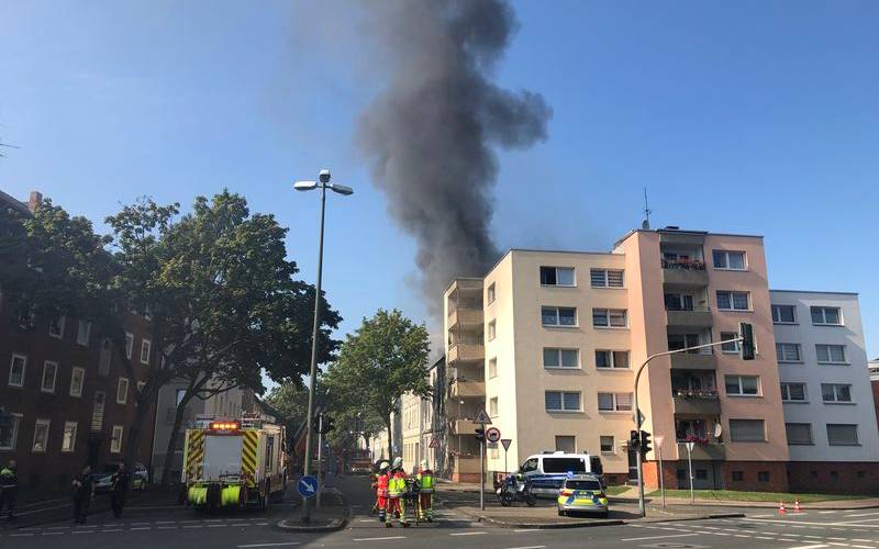 Ein Einsatzort der Feuerwehr in Gelsenkirchen-Schalke. Zu sehen sind eine hohe Rauchsäule, eine mehrstöckiges Gebäude sowie Polize- und Feuerwehreinsatzkräfte