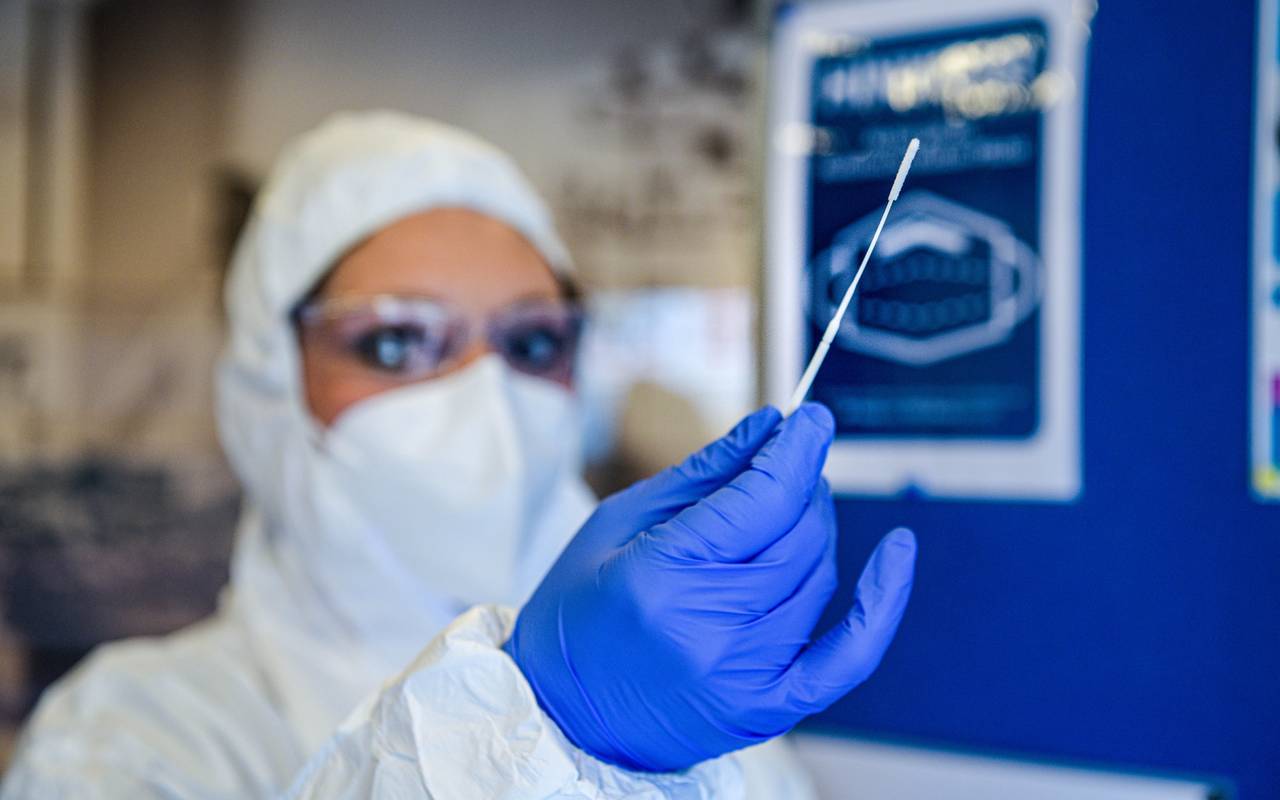 Eine vermummte Frau hält ein Teststäbchen hoch