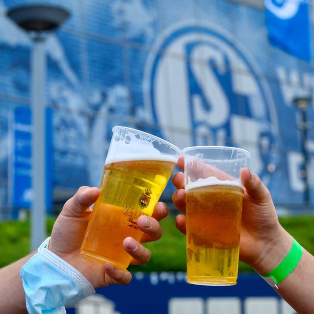 Zwei Schalke-Fans stoßen vor der Veltins-Arena mit Bierbechern aus Plastik an