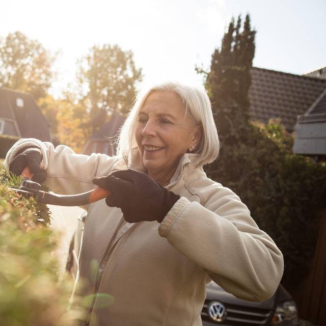 Eine ältere Dame schneidet eine Hecke