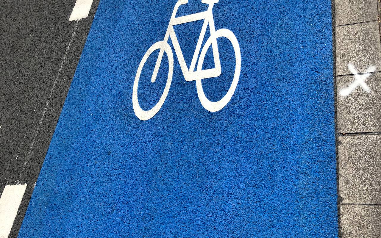 Ein blauer Schutzstreifen auf einer Straße mit Fahrrad (in weiß)
