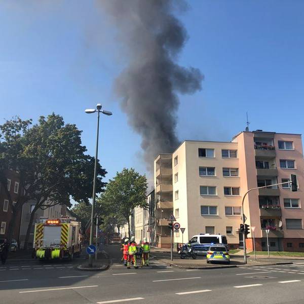 Ein Einsatzort der Feuerwehr in Gelsenkirchen-Schalke. Zu sehen sind eine hohe Rauchsäule, eine mehrstöckiges Gebäude sowie Polize- und Feuerwehreinsatzkräfte