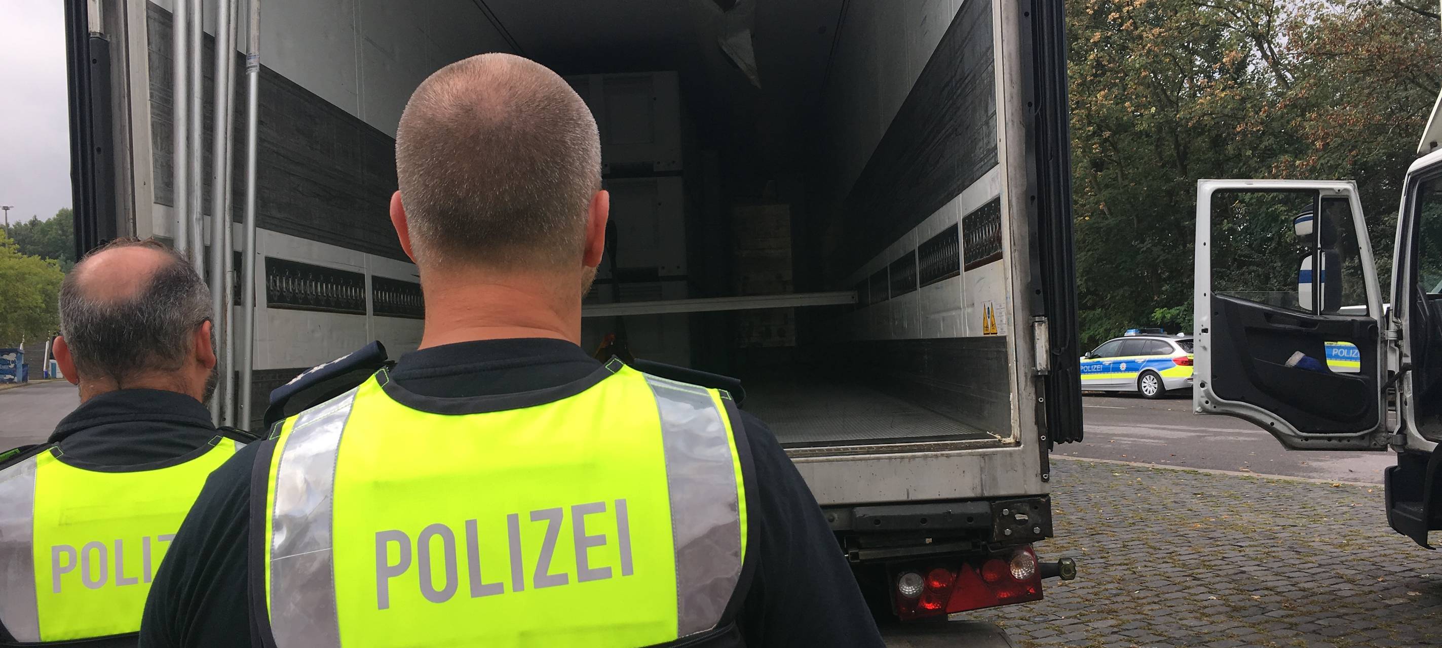 Zwei Polizeibeamten kontrollieren die Ladefläche eines LKWs.