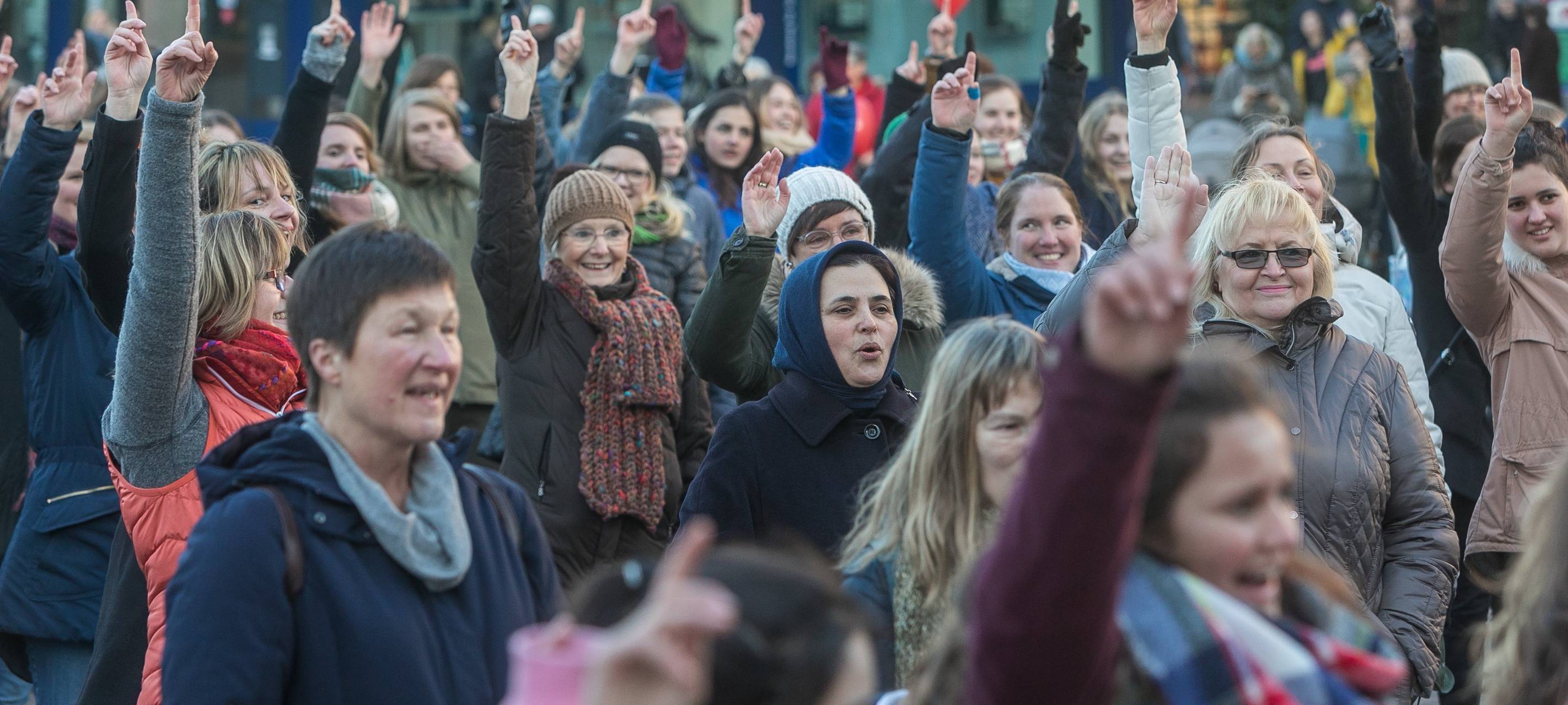 Frauen stehen auf einem Platz und recken gleichzeitig eine Hand in die Luft
