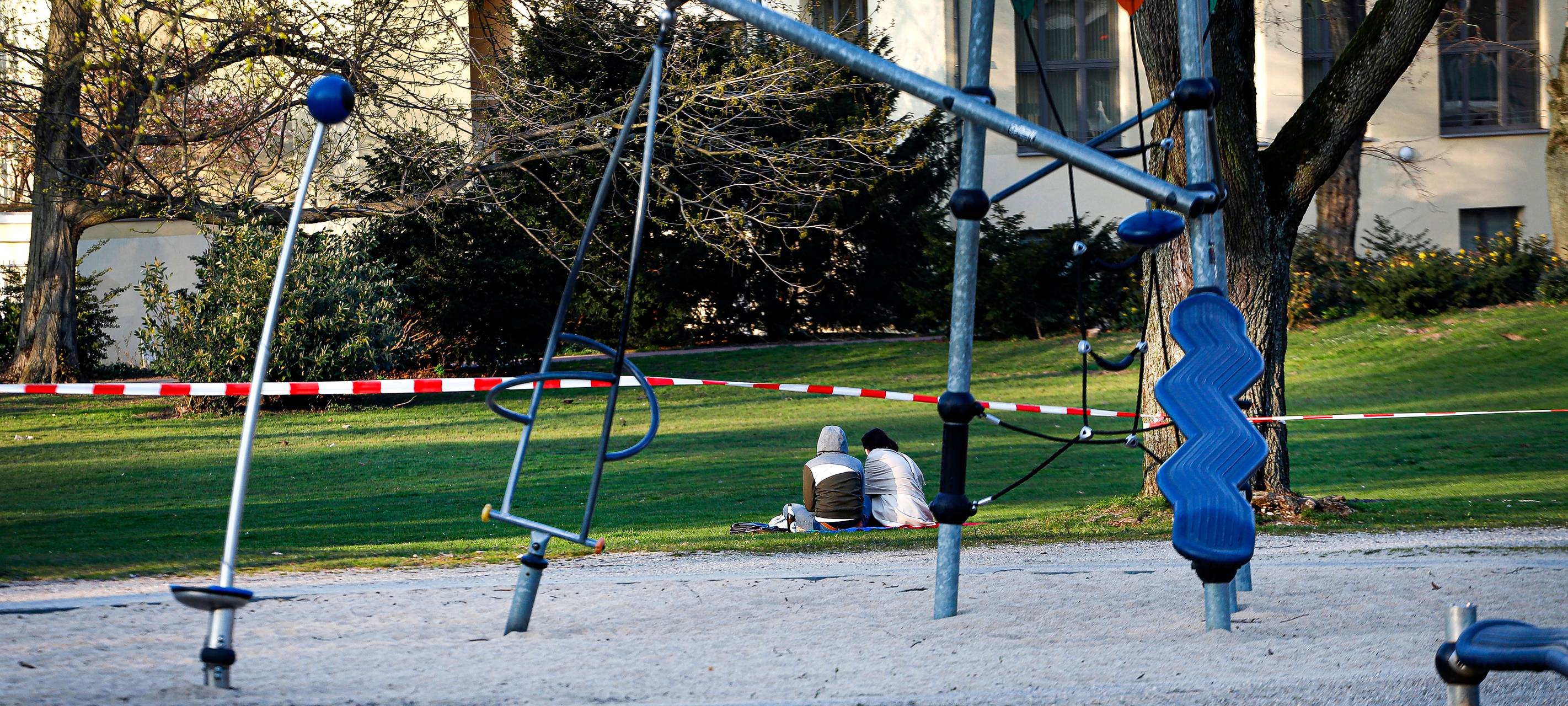 Zwei Frauen sitzen im Bereich eines abgesperrten Spielplatzes