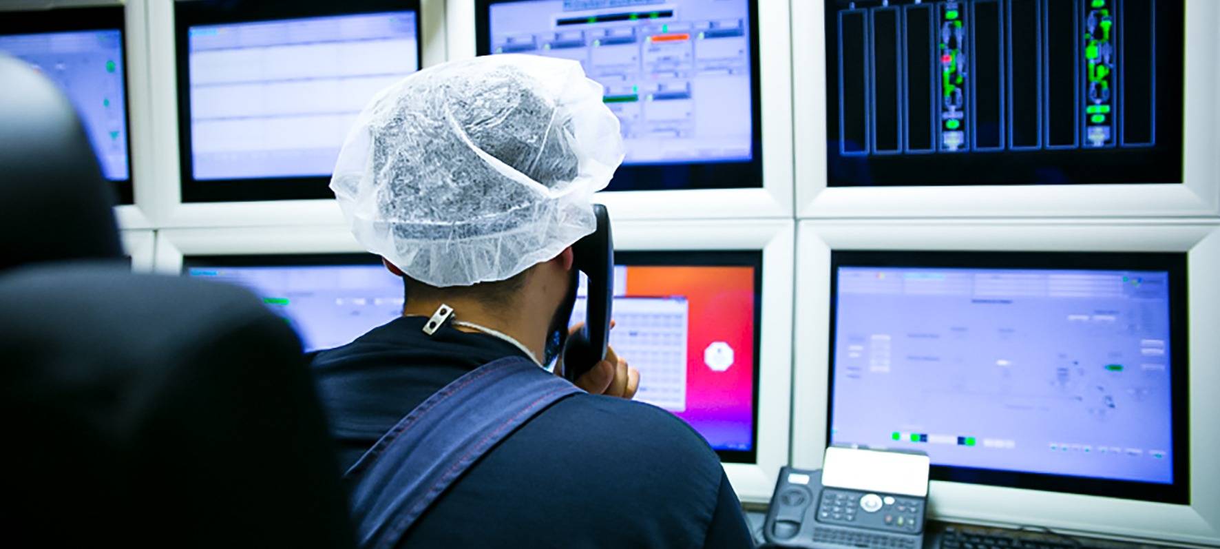 Mitarbeiter in einer Lebensmittelfirma sitzt vor Bildschirmen, die eine Maschine steuern