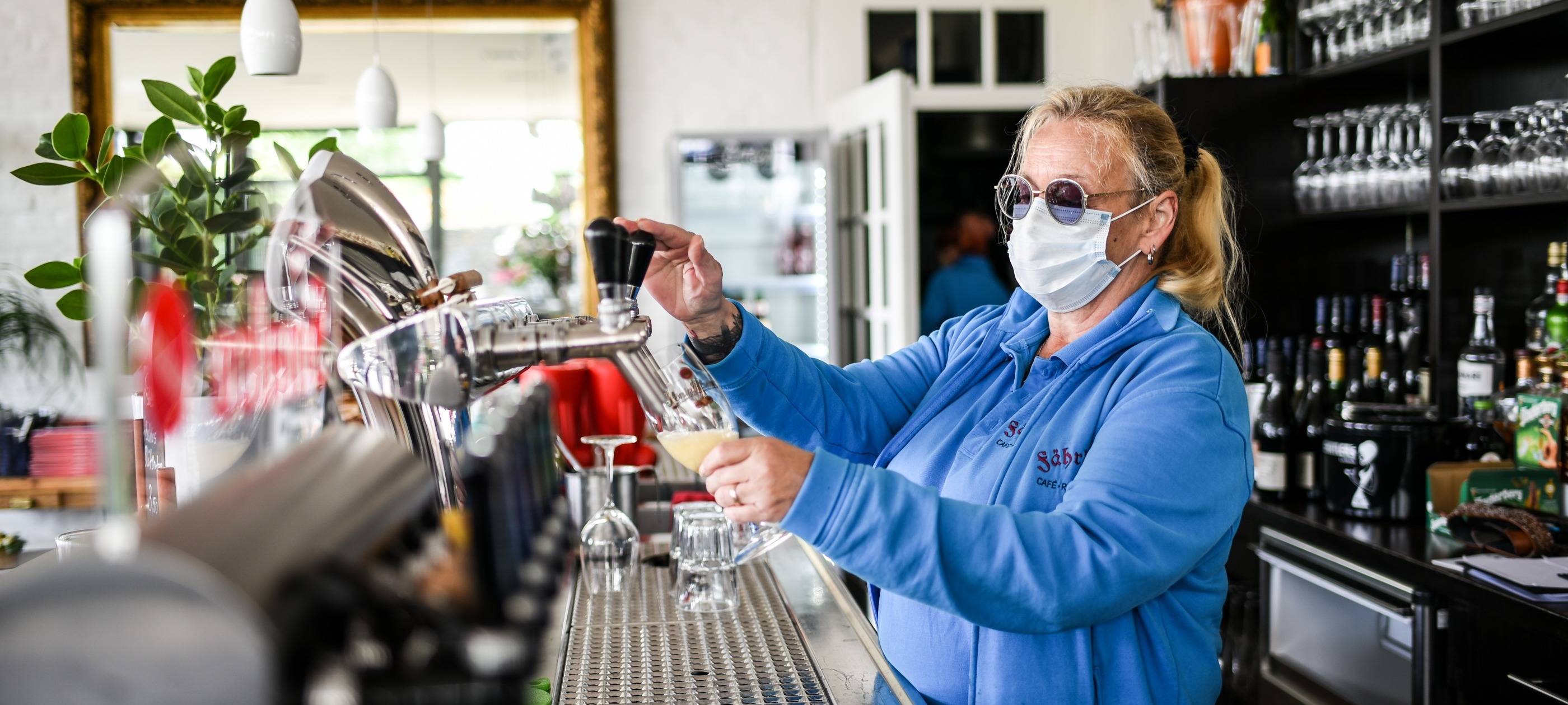Gastwirtin zapft Bier mit Maske