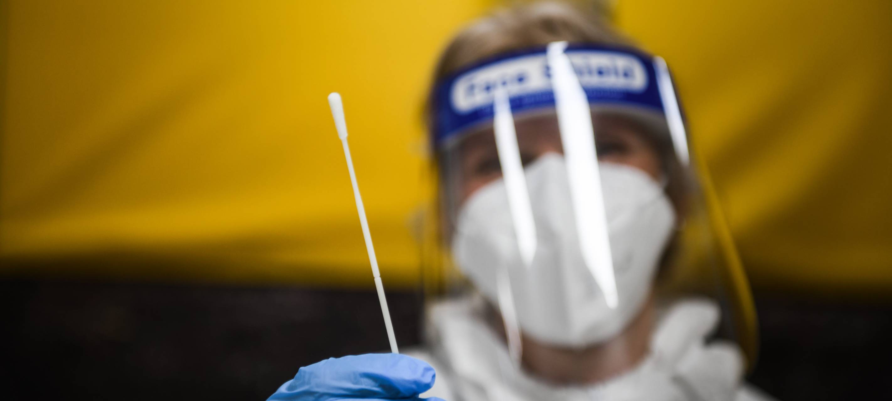 Eine vermummte Frau hält ein Teststäbchen hoch