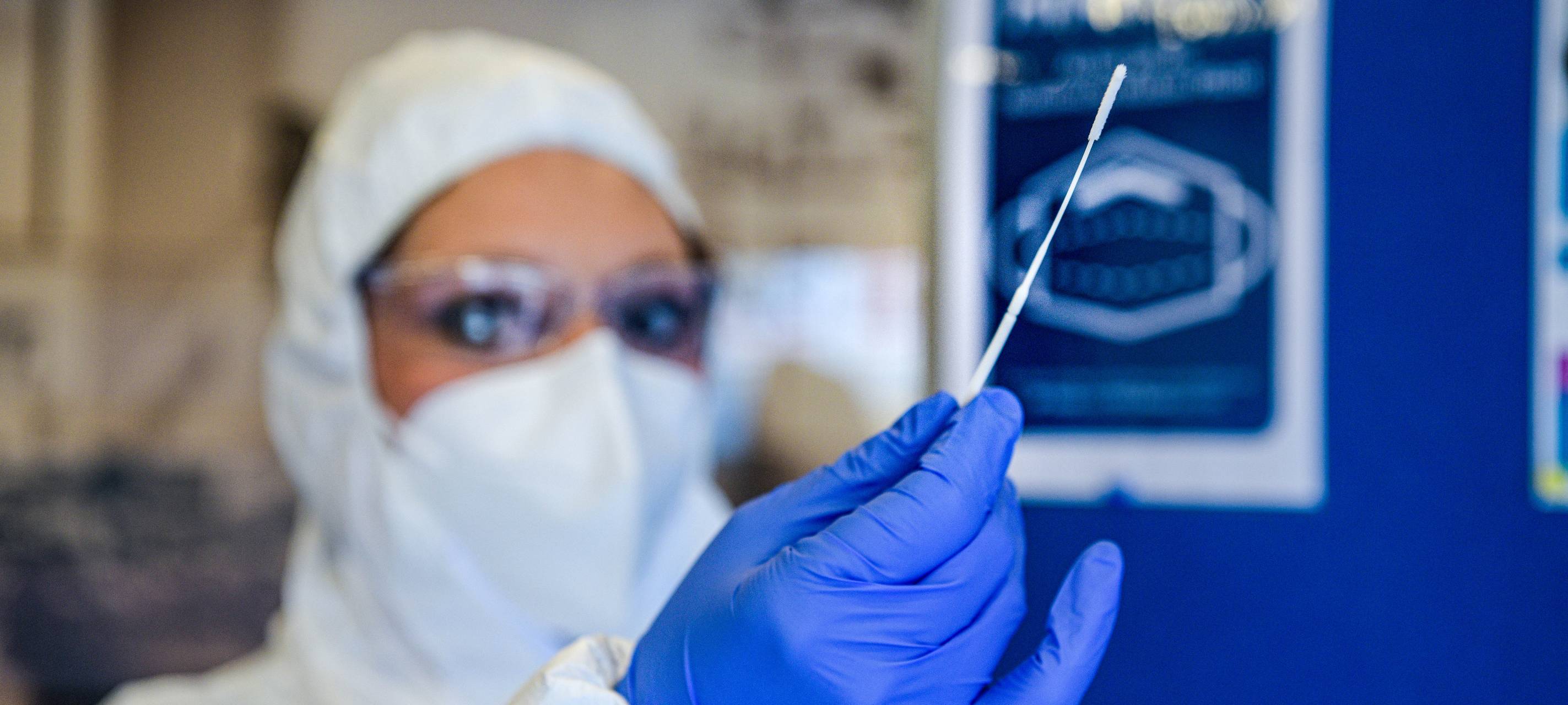 Eine vermummte Frau hält ein Teststäbchen hoch