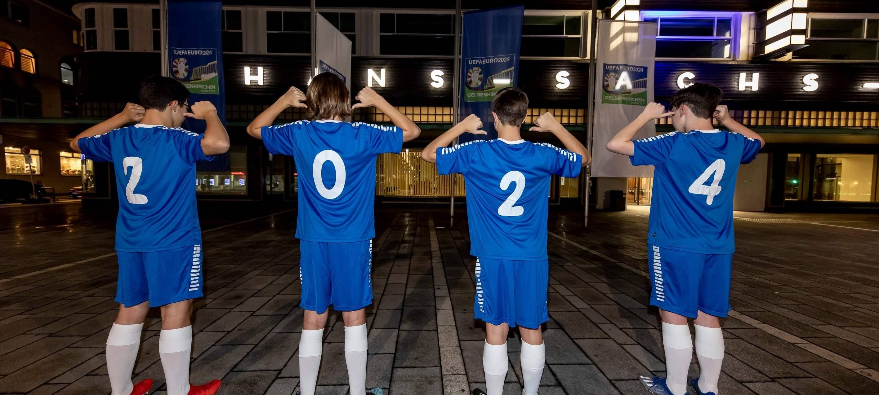 Kinder mit blauen Trikots und der Zahl 2024 stehen vor dem Hans-Sachs-Haus