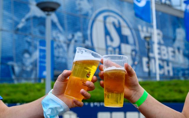 Zwei Schalke-Fans stoßen vor der Veltins-Arena mit Bierbechern aus Plastik an