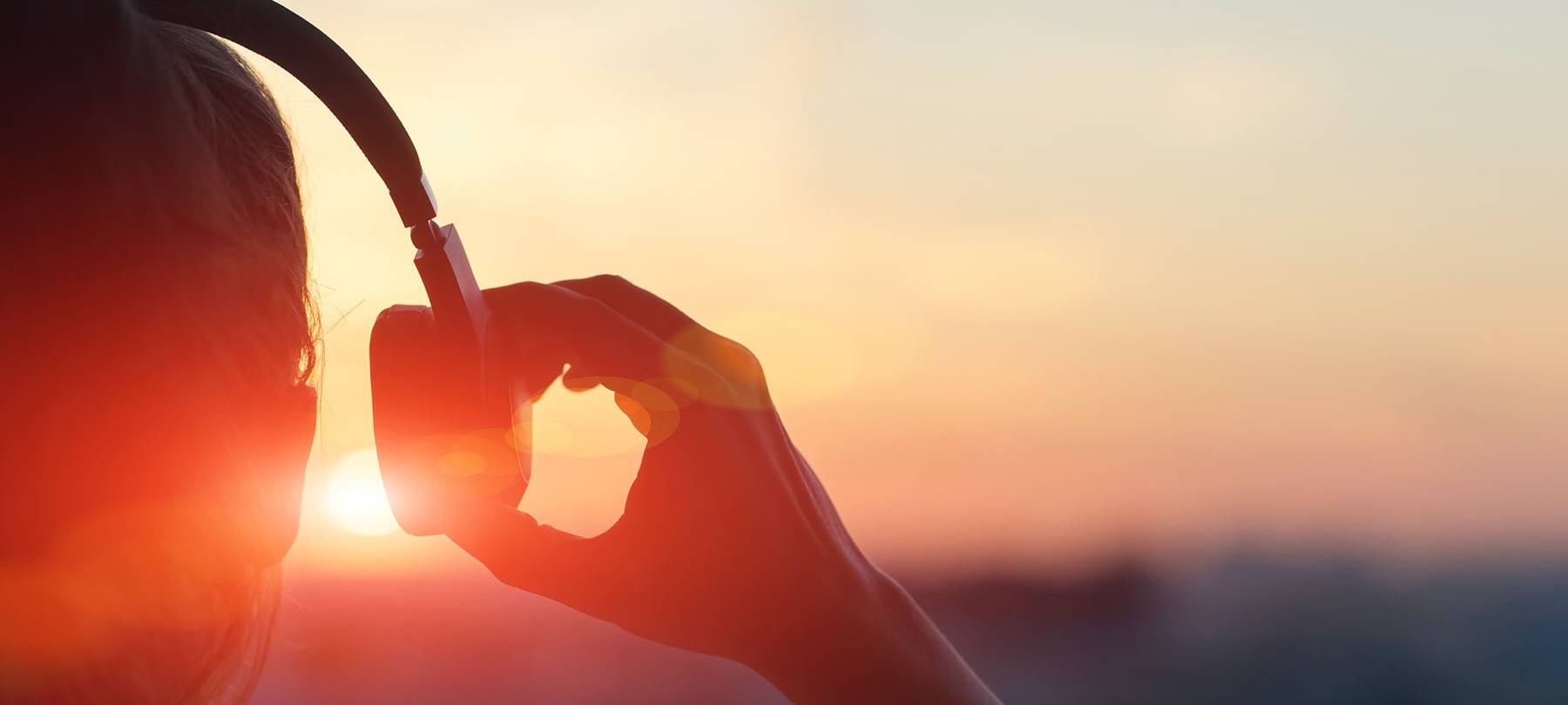 Frau mit Kopfhörern vor Sonnenuntergang
